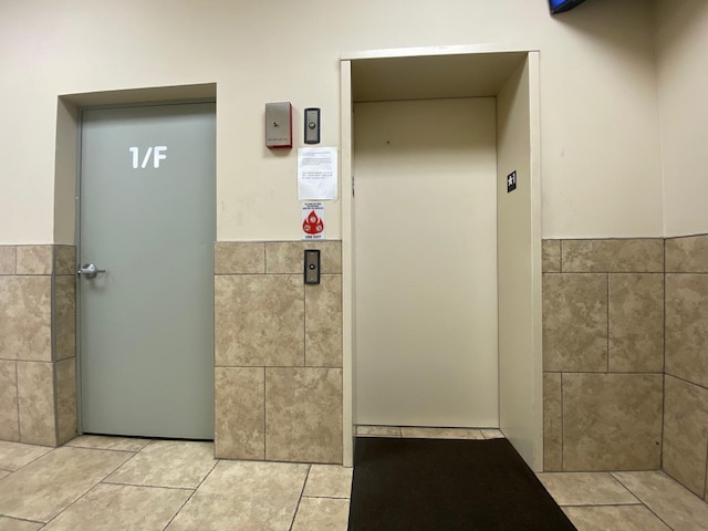 interior space with elevator, tile patterned flooring, and tile walls