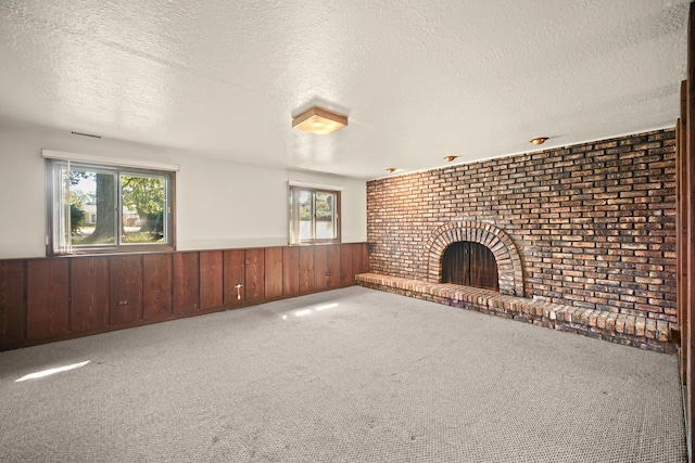 unfurnished living room with wood walls, a textured ceiling, a wealth of natural light, and a brick fireplace