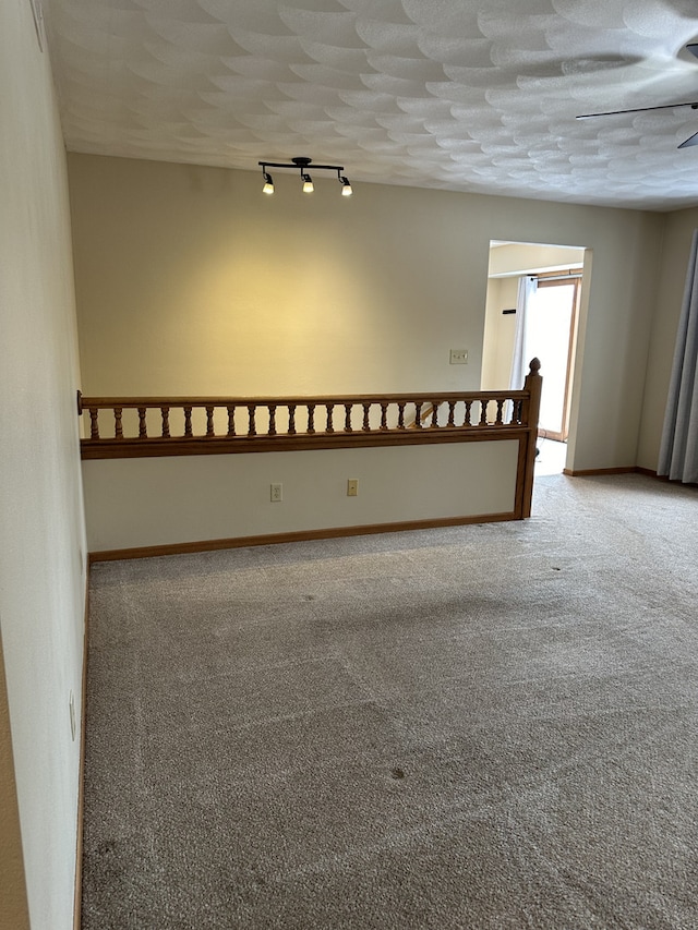 empty room featuring a textured ceiling, carpet floors, and track lighting