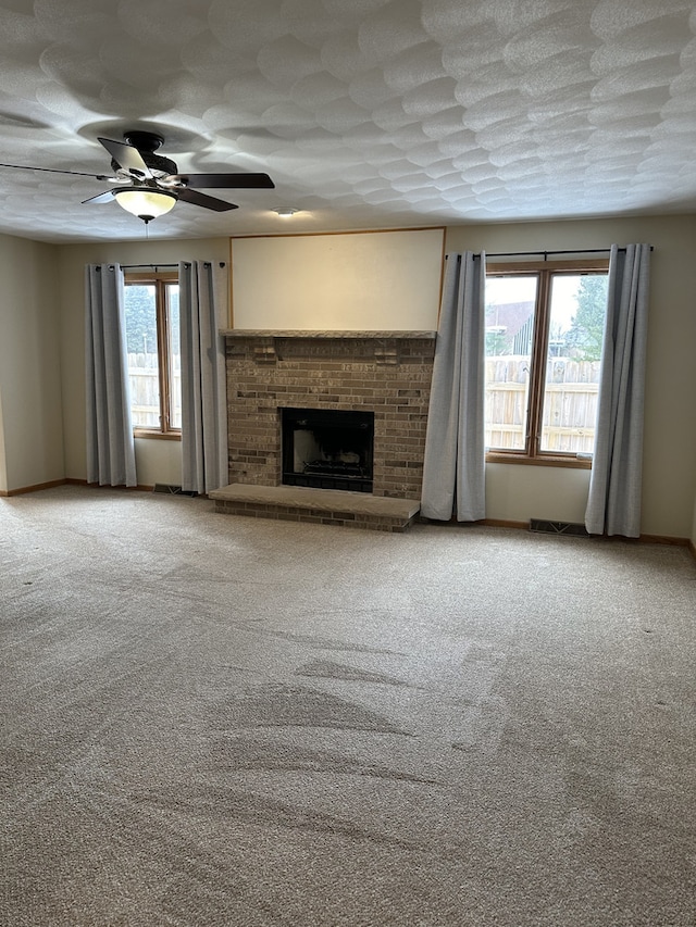 unfurnished living room with ceiling fan, carpet floors, a textured ceiling, and a brick fireplace