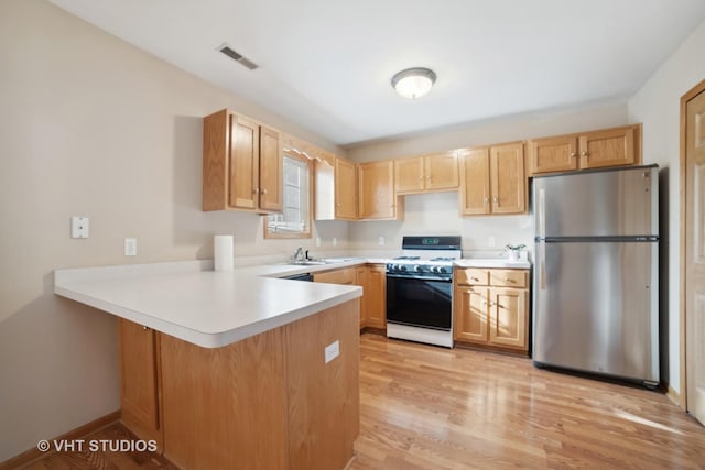 kitchen with kitchen peninsula, light wood-type flooring, light brown cabinets, white range with gas stovetop, and stainless steel refrigerator