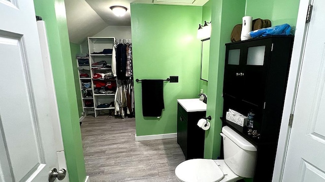 bathroom with toilet, vanity, hardwood / wood-style flooring, and vaulted ceiling