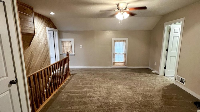 interior space with ceiling fan, wood walls, a textured ceiling, lofted ceiling, and dark carpet