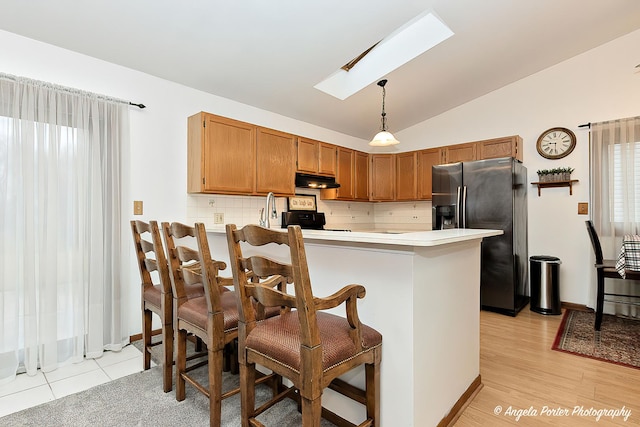 kitchen with lofted ceiling with skylight, hanging light fixtures, stainless steel fridge, a kitchen bar, and kitchen peninsula