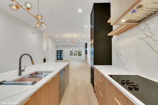 kitchen featuring black electric stovetop, decorative light fixtures, light stone countertops, and sink