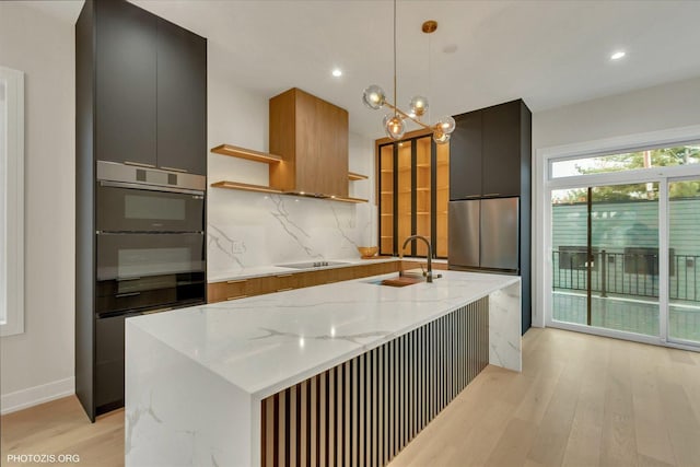 kitchen with pendant lighting, sink, light stone counters, and a center island with sink