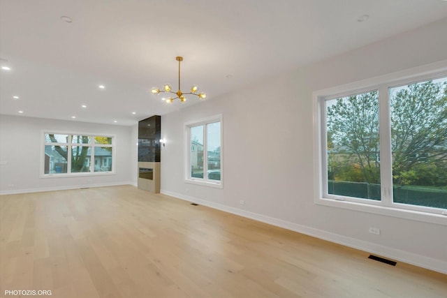 unfurnished living room with an inviting chandelier and light hardwood / wood-style floors