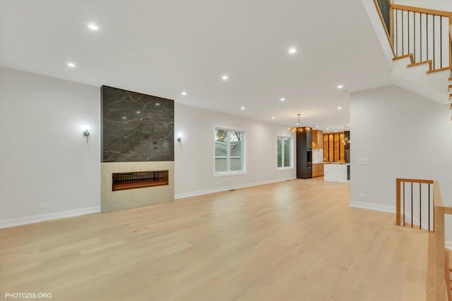 unfurnished living room featuring a high end fireplace, a chandelier, and light hardwood / wood-style floors