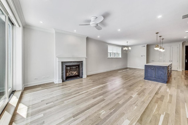 unfurnished living room with crown molding, a tile fireplace, ceiling fan with notable chandelier, and light hardwood / wood-style flooring