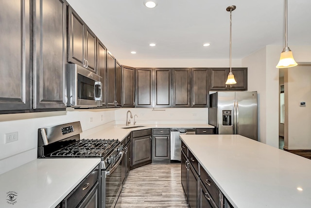 kitchen featuring dark brown cabinets, stainless steel appliances, sink, decorative light fixtures, and light hardwood / wood-style floors