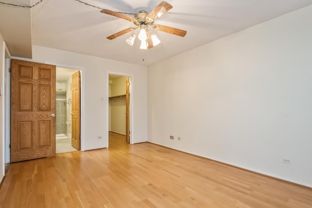 unfurnished bedroom with light wood-type flooring, ceiling fan, a spacious closet, connected bathroom, and a closet