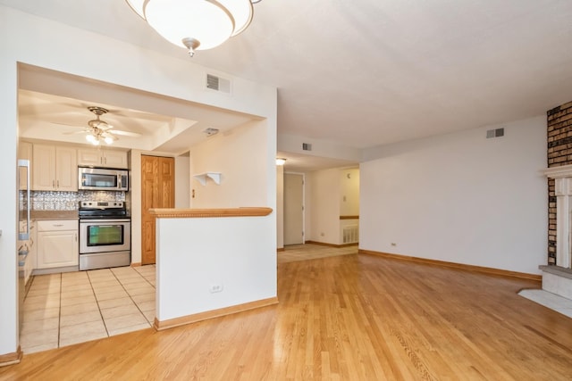 kitchen featuring tasteful backsplash, a brick fireplace, stainless steel appliances, ceiling fan, and light hardwood / wood-style flooring