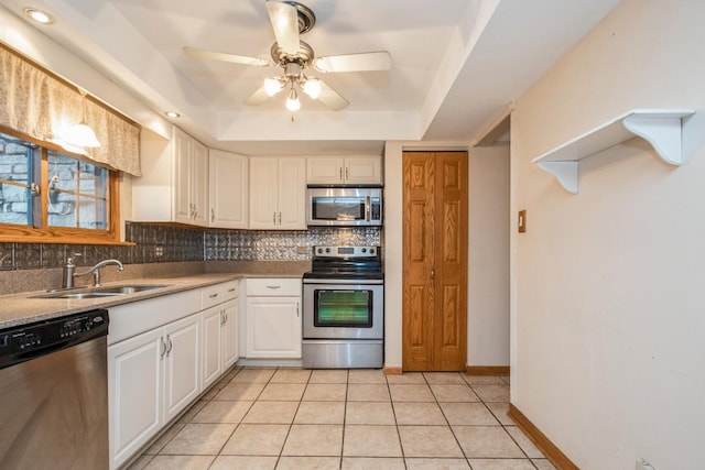 kitchen with sink, stainless steel appliances, light tile patterned floors, a tray ceiling, and white cabinets