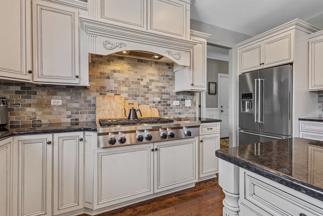 kitchen with appliances with stainless steel finishes, decorative backsplash, dark stone countertops, and custom range hood