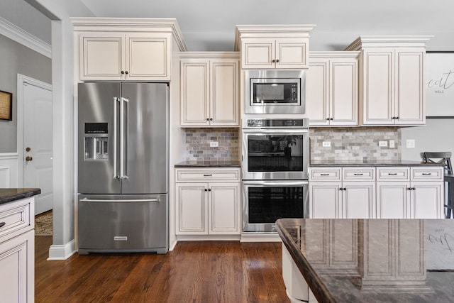 kitchen featuring tasteful backsplash, dark stone counters, appliances with stainless steel finishes, ornamental molding, and dark hardwood / wood-style flooring