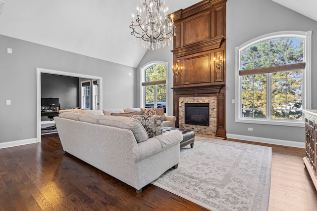 living room featuring dark wood-type flooring, a chandelier, a fireplace, and high vaulted ceiling