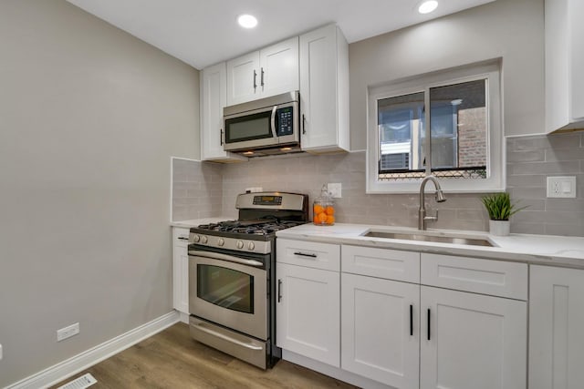 kitchen with decorative backsplash, appliances with stainless steel finishes, light wood-type flooring, sink, and white cabinetry