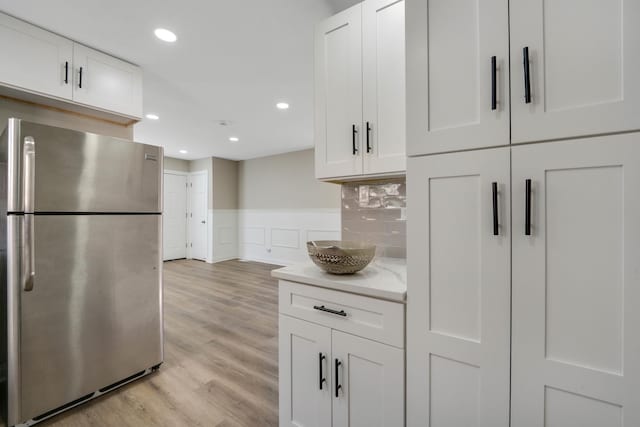 kitchen featuring decorative backsplash, stainless steel fridge, white cabinets, and light hardwood / wood-style floors