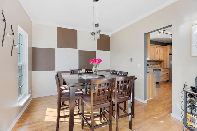 dining space with crown molding, rail lighting, a wealth of natural light, and light hardwood / wood-style flooring