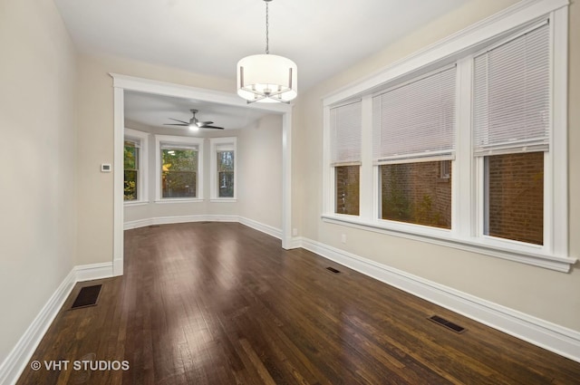 unfurnished dining area with ceiling fan with notable chandelier and dark wood-type flooring