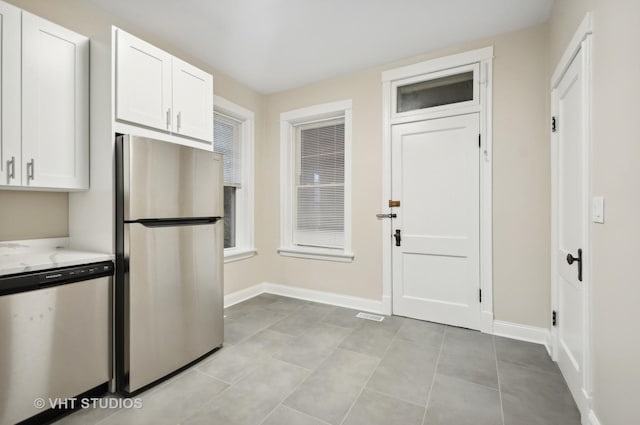 kitchen with light tile patterned flooring, appliances with stainless steel finishes, white cabinetry, and light stone countertops