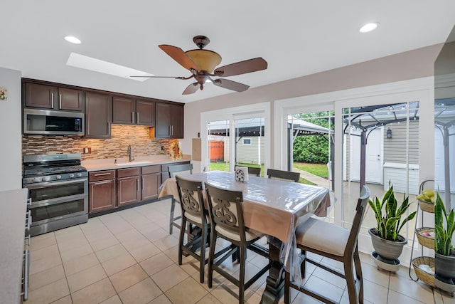 kitchen featuring a skylight, sink, stainless steel appliances, tasteful backsplash, and dark brown cabinets