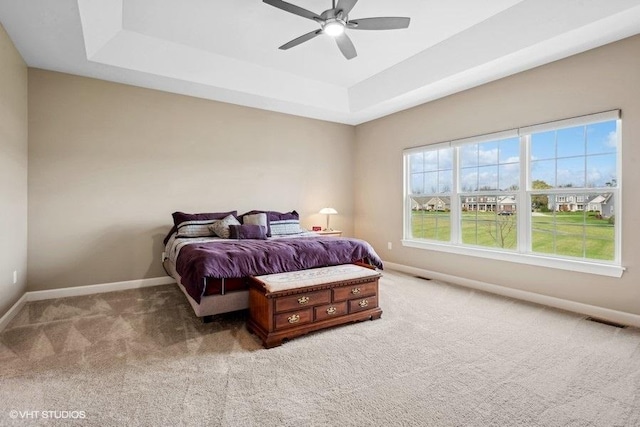 bedroom with ceiling fan, light colored carpet, and a tray ceiling