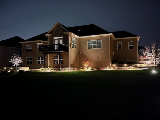 back house at twilight featuring a balcony and a lawn