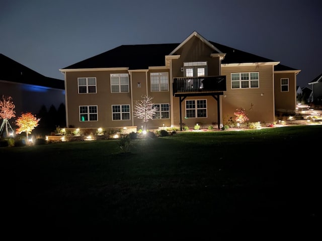 back house at night featuring a lawn and a balcony