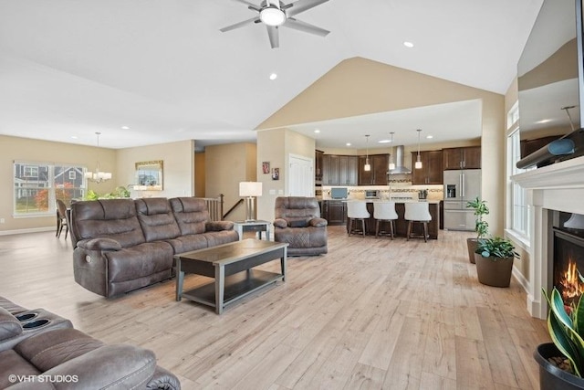 living room featuring vaulted ceiling, light hardwood / wood-style flooring, and ceiling fan with notable chandelier