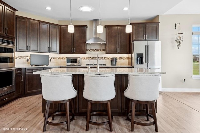 kitchen with hanging light fixtures, a kitchen island with sink, and wall chimney exhaust hood