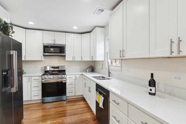 kitchen with sink, light wood-type flooring, appliances with stainless steel finishes, light stone counters, and white cabinetry