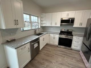 kitchen with white cabinets, stainless steel appliances, light stone countertops, and sink