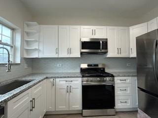 kitchen featuring white cabinets, sink, appliances with stainless steel finishes, tasteful backsplash, and light stone counters