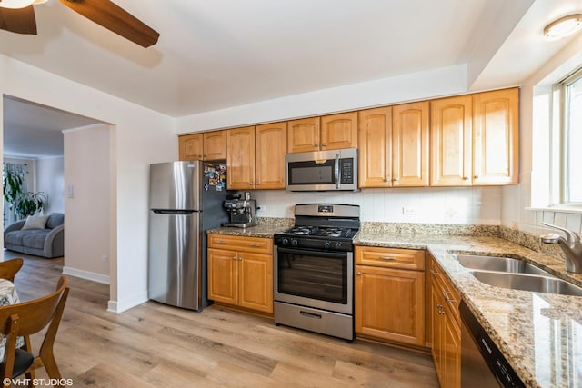 kitchen featuring light stone countertops, light wood-type flooring, stainless steel appliances, ceiling fan, and sink