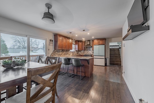 kitchen featuring kitchen peninsula, tasteful backsplash, wall chimney exhaust hood, sink, and white refrigerator