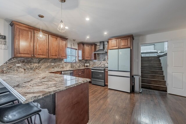 kitchen featuring sink, wall chimney exhaust hood, decorative backsplash, appliances with stainless steel finishes, and a kitchen bar