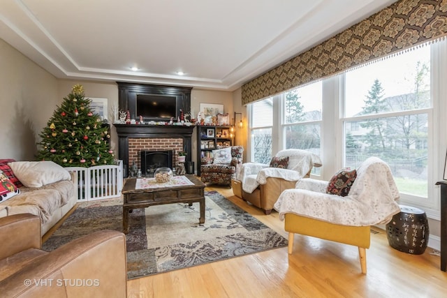 living room with a raised ceiling, hardwood / wood-style flooring, and a brick fireplace