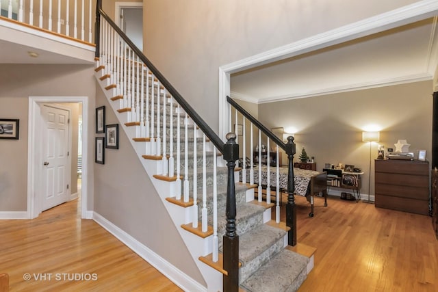 staircase with hardwood / wood-style floors, a towering ceiling, and ornamental molding