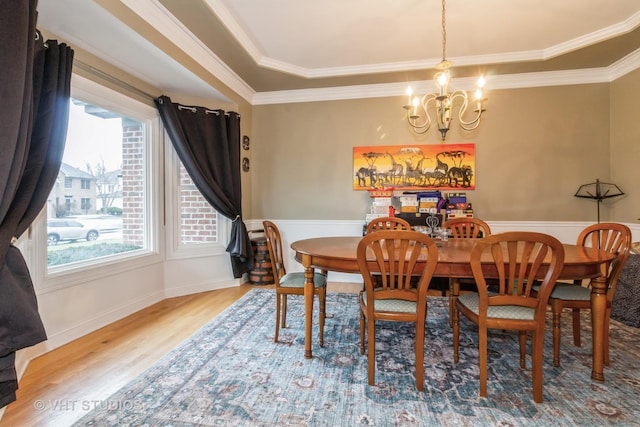 dining area with a raised ceiling, hardwood / wood-style flooring, an inviting chandelier, and crown molding