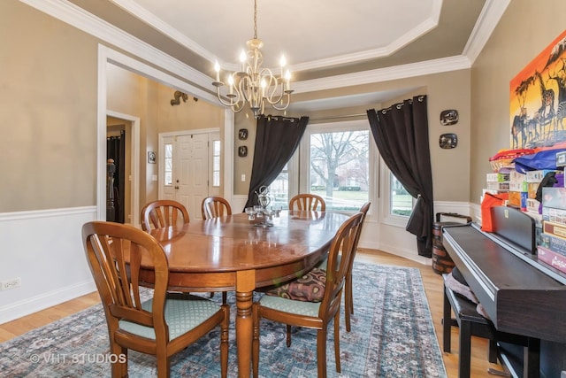 dining room featuring a notable chandelier, light wood-type flooring, ornamental molding, and a tray ceiling