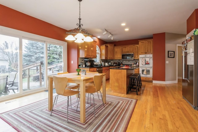 kitchen with a breakfast bar, light wood-type flooring, decorative light fixtures, a kitchen island, and stainless steel appliances