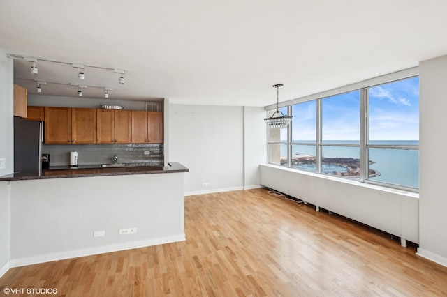 kitchen with a water view, hanging light fixtures, decorative backsplash, stainless steel fridge, and light hardwood / wood-style floors