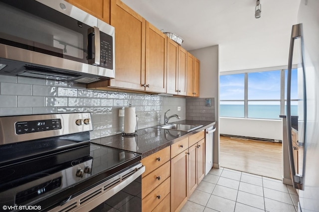 kitchen featuring sink, light tile patterned floors, dark stone counters, a water view, and appliances with stainless steel finishes