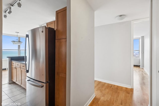 kitchen with a water view, stainless steel refrigerator, hanging light fixtures, and light hardwood / wood-style floors