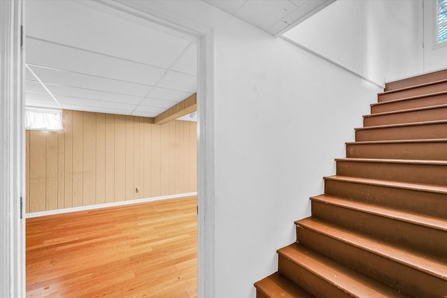 stairs with hardwood / wood-style floors, a paneled ceiling, and wooden walls