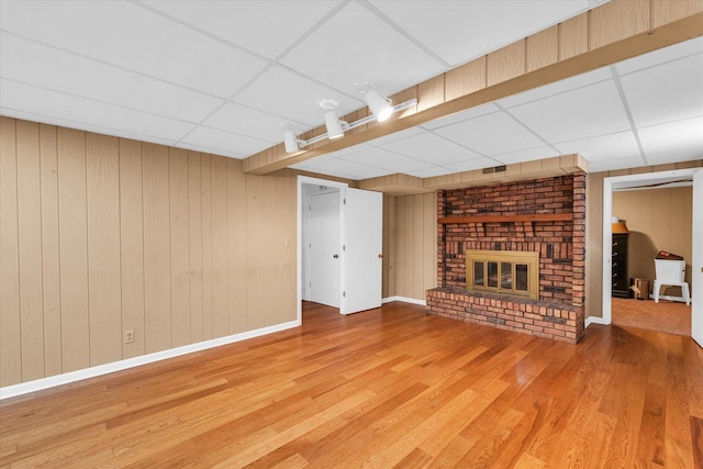 unfurnished living room featuring a paneled ceiling, wood walls, a fireplace, and hardwood / wood-style flooring