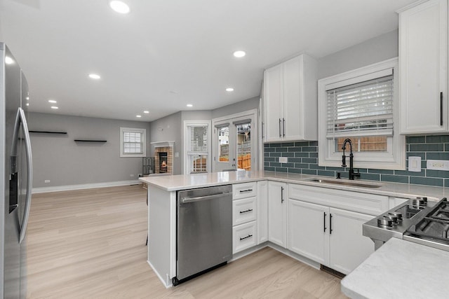 kitchen with sink, stainless steel appliances, kitchen peninsula, white cabinets, and light wood-type flooring