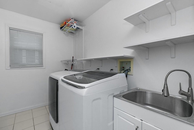 clothes washing area with washing machine and dryer, sink, light tile patterned flooring, and cabinets