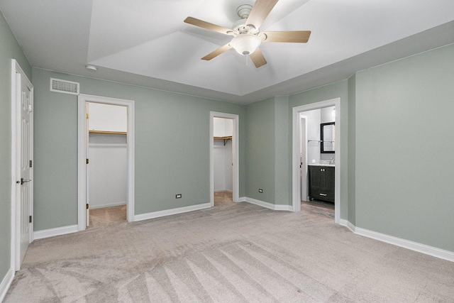 unfurnished bedroom featuring a walk in closet, ensuite bath, light colored carpet, ceiling fan, and a closet